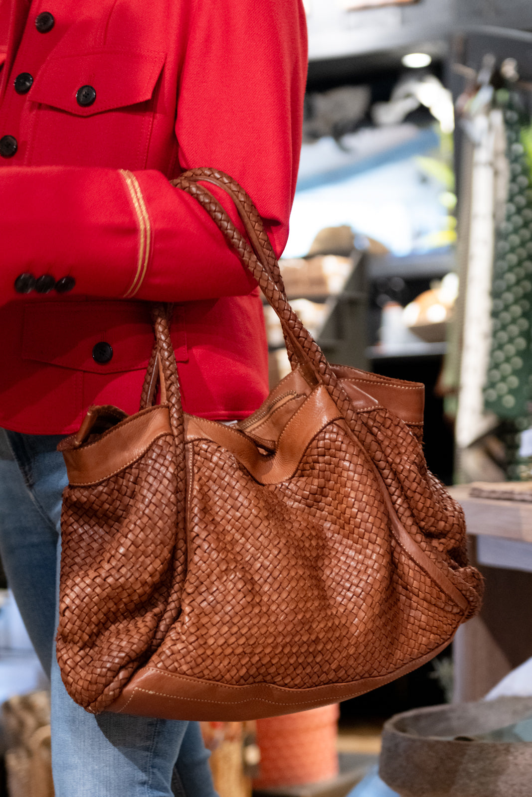 Woven tan handbag being worn on the arm of a lady in a red jacket shopping 